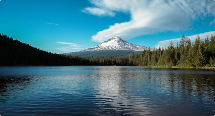 blue sky with tall mountain, white clouds, and forest surrounding a blue lake